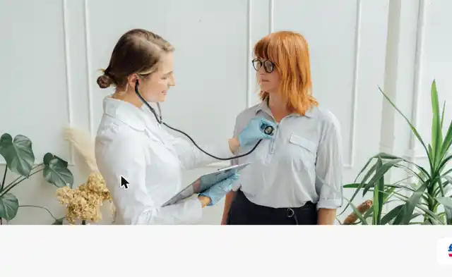 Heilpraktikerin in weißem Kittel hört mit einem Stethoskop den Brustkorb einer Patientin ab, im Hintergrund Grünpflanzen
