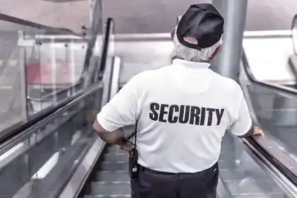 Security guard in uniform seen from behind on an escalator, radio on his belt
